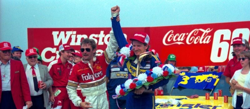 Dale Earnhardt (right) celebrates his first Coca-Cola 600 victory in 1986 alongside runner-up Tim Richmond (left), conquering his home track of Charlotte Motor Speedway. 