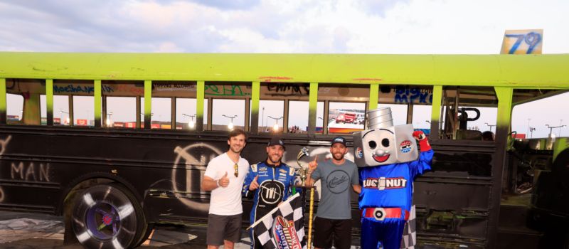 Trackhouse Racing mechanic James Civali poses with drivers Daniel Suarez, Ross Chastain and Charlotte Motor Speedway mascot, Lugnut, after claiming victory in the Cook Out Summer Shootout Champions’ Night school bus race.