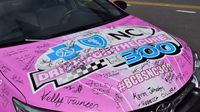 Signatures of breast cancer survivors fill the hood of a bright pink Drive for the Cure 300 pace car during a Laps Around Uptown event in Center City Charlotte Monday to kick off race week at Charlotte Motor Speedway.